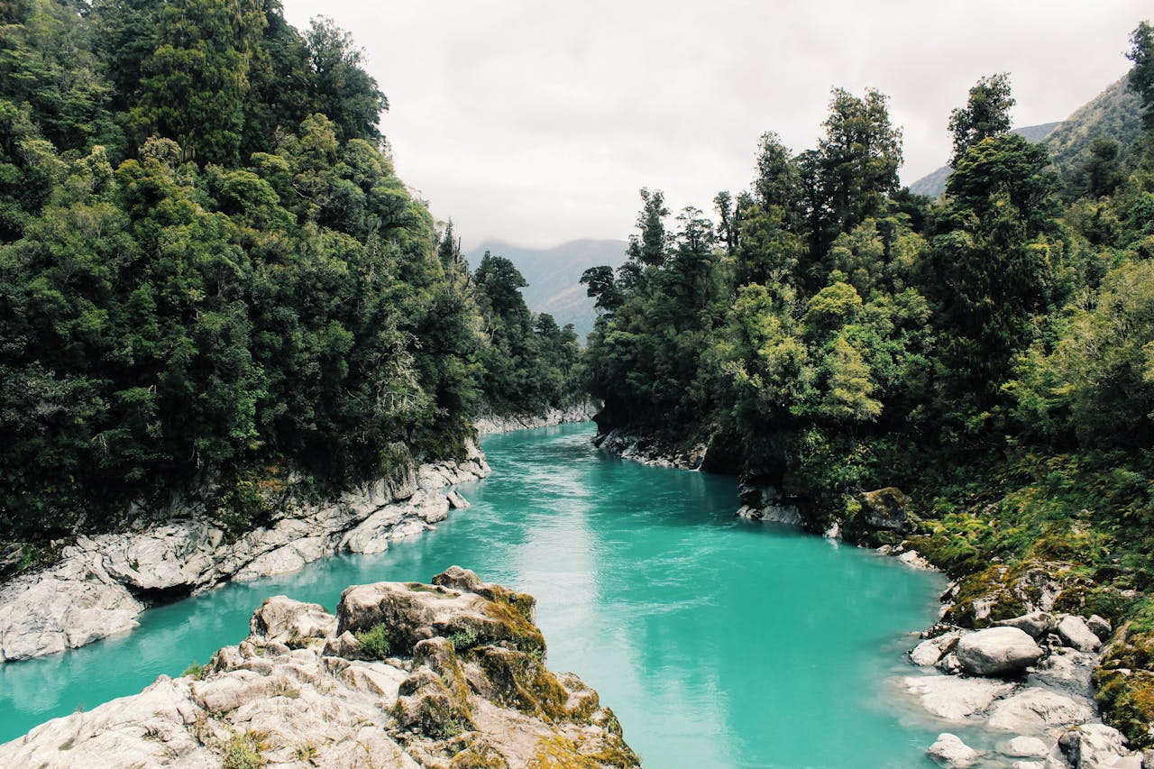 our-story-01 Beautiful turquoise river winding through a dense, lush forest under a cloudy sky.