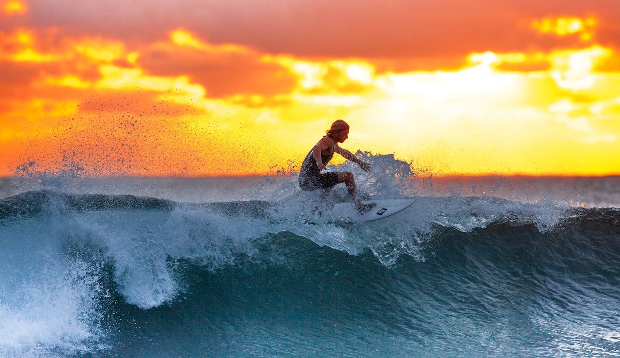 about-01 Surfer riding a wave during a stunning sunset, capturing the thrill of water sports.