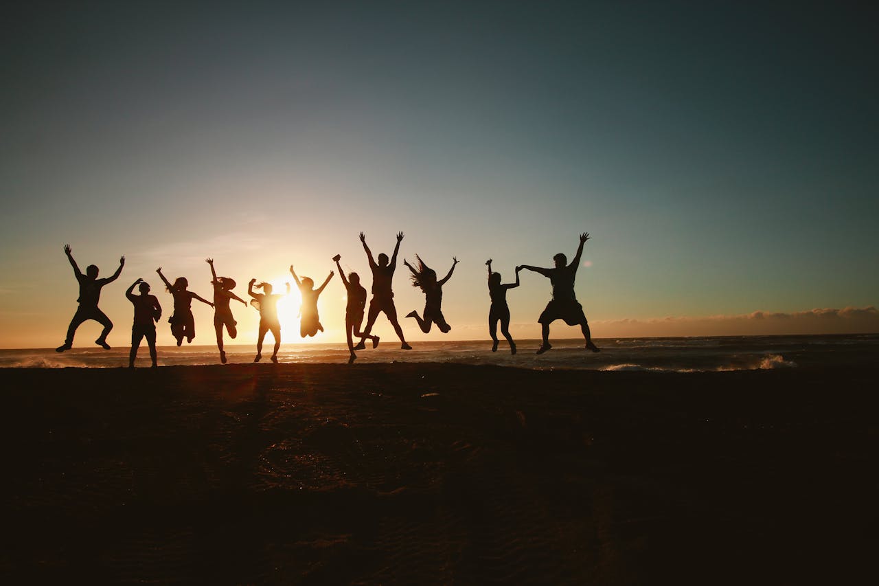 services-02 Silhouette of a group of friends jumping on a beach at sunset, expressing joy and freedom.