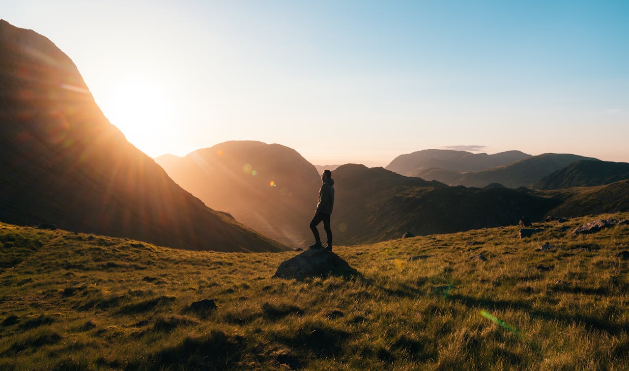 about-03 Silhouette of a person standing on a hill during sunrise in Cumbria, England with scenic mountain views.