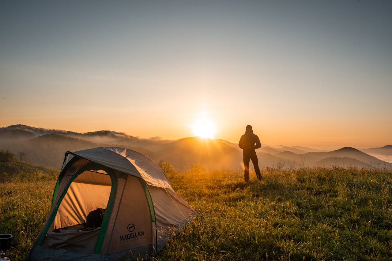 mission-02 A camper enjoys the sunrise in a mountain setting with a tent. Perfect nature escape.